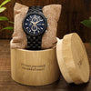 Black wristwatch with blue face in a wooden box on a wooden surface