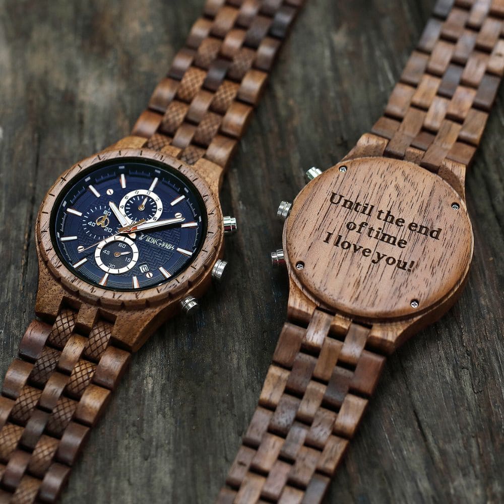 Two wooden watches on a dark wooden surface with one displaying an engraved message.