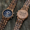 Two wooden watches on a dark wooden surface with one displaying an engraved message.
