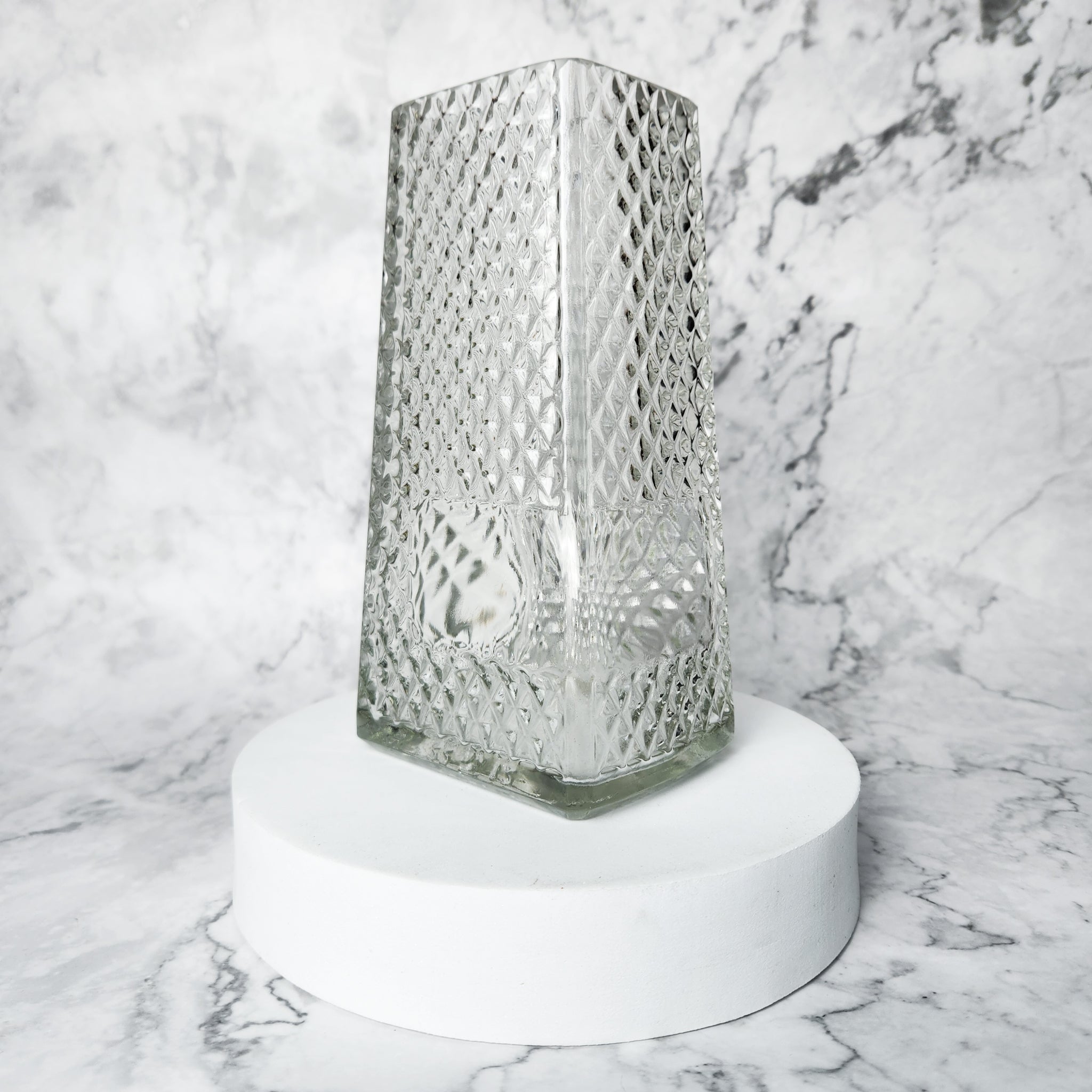 Decorative glass vase on a white pedestal against a marble background