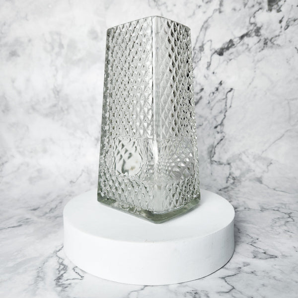 Decorative glass vase on a white pedestal against a marble background