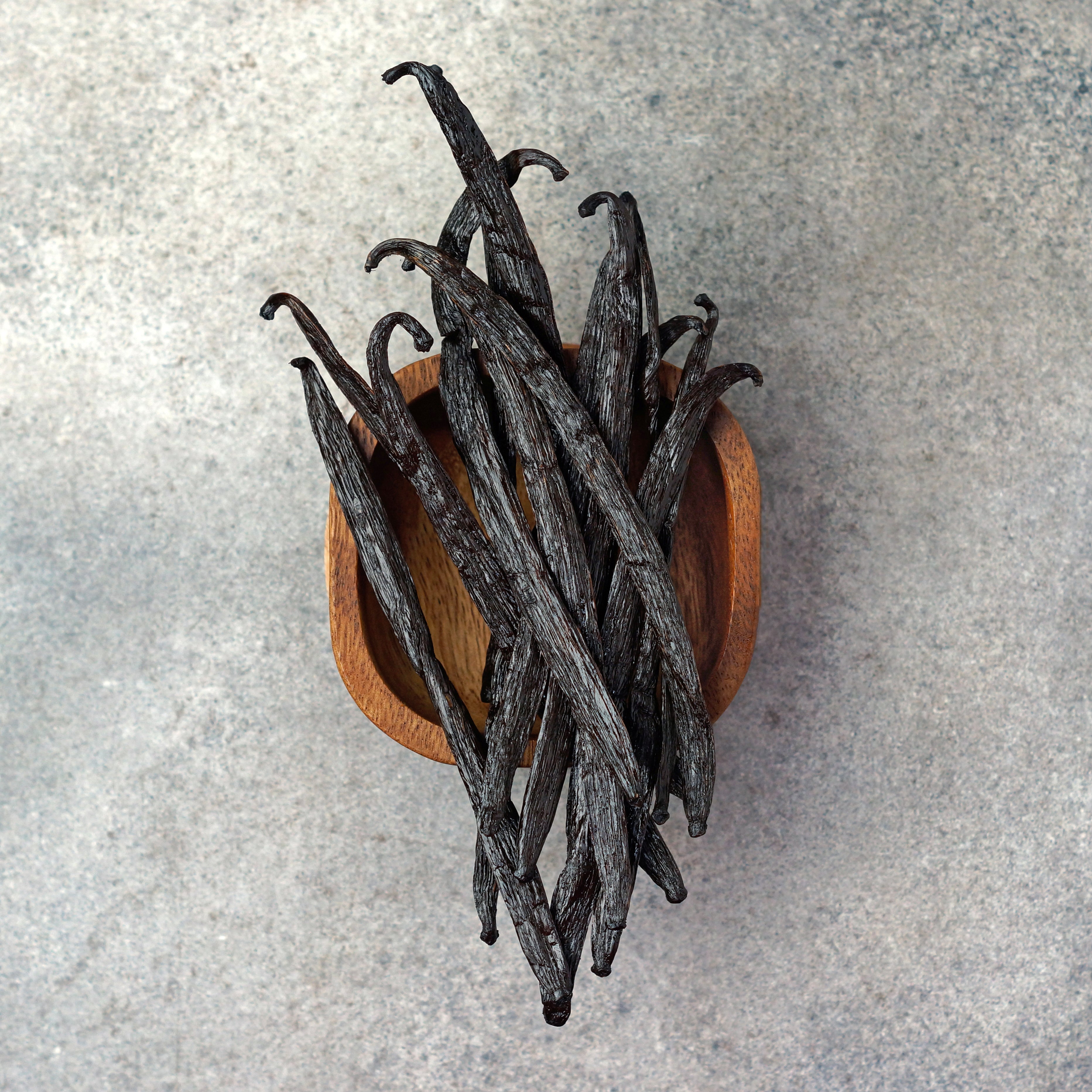 Vanilla beans in a wooden bowl on a gray surface