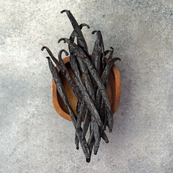 Vanilla beans in a wooden bowl on a gray surface