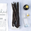 Vanilla beans on a white surface with a bottle and dropper, and a measuring chart.