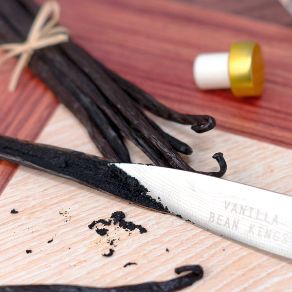 Vanilla beans and a vanilla bean press on a wooden surface