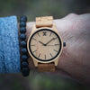 Wooden watch with cork strap on wrist against a blurred natural background