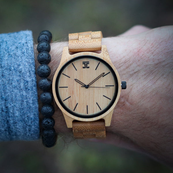 Wooden watch with cork strap on wrist against a blurred natural background