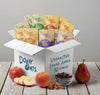 Box of Dolly Oats vegan no sugar added oat packages with fruits and a bowl of raisins on a wooden surface.
