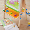 Children's art easel with drawing on a wooden floor, surrounded by art supplies.