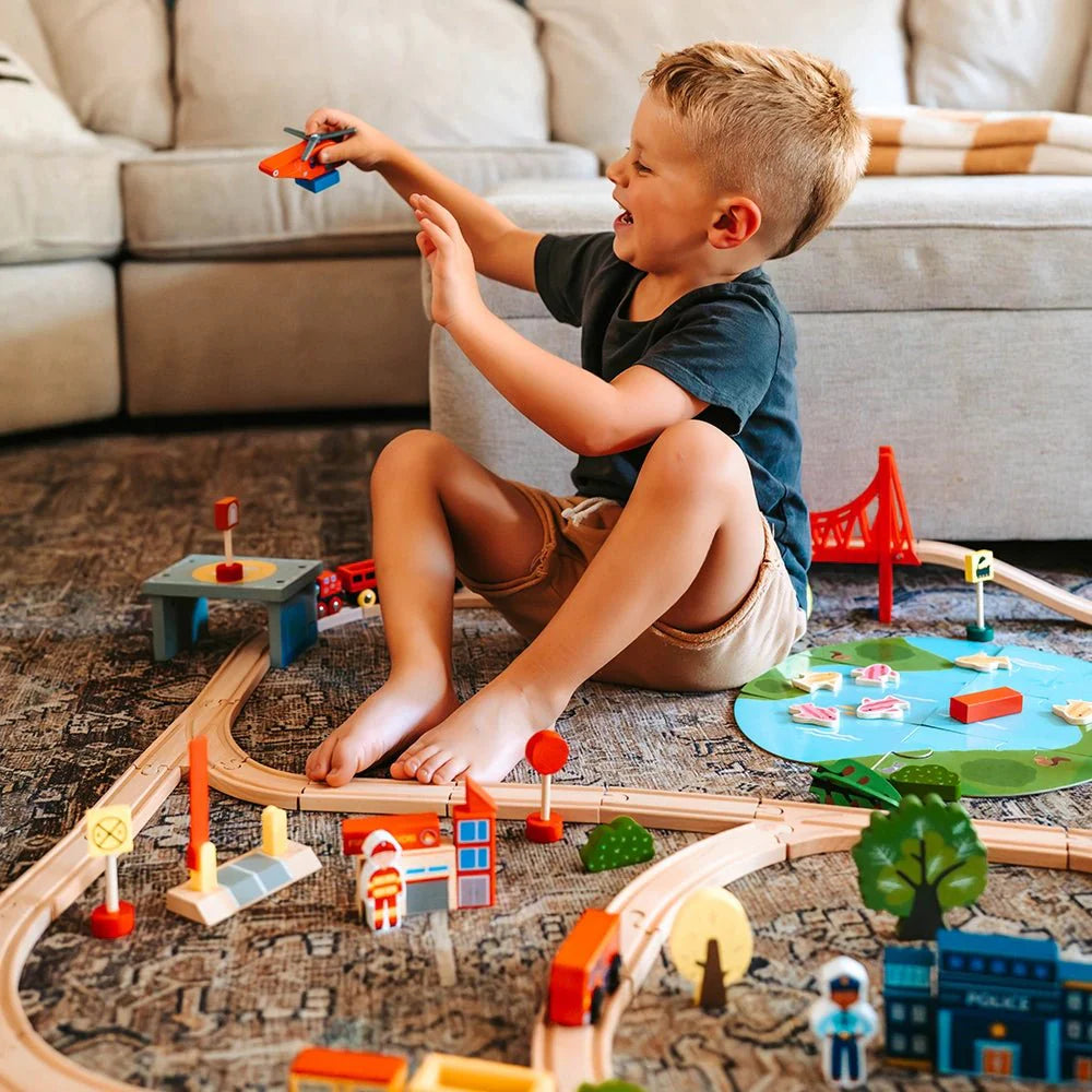 Child playing with a wooden toy train set on the floor.