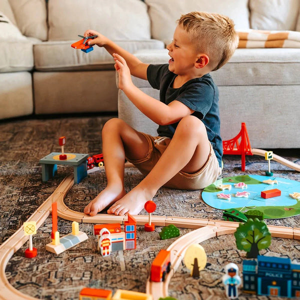 Child playing with a wooden toy train set on the floor.