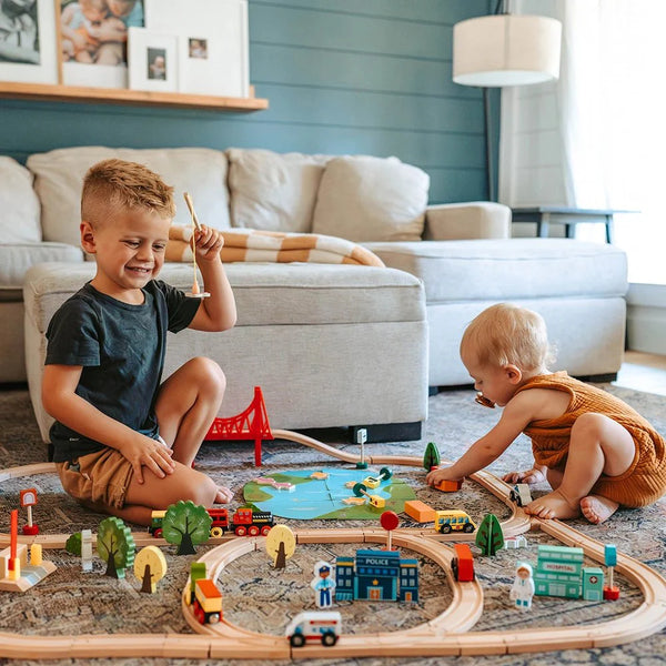 Two children playing with a wooden train set in a living room.