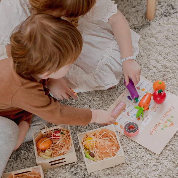 Two children playing with toy fruits and vegetables on a carpeted floor.