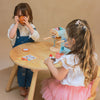 Two children playing with toys at a wooden table against a beige wall.