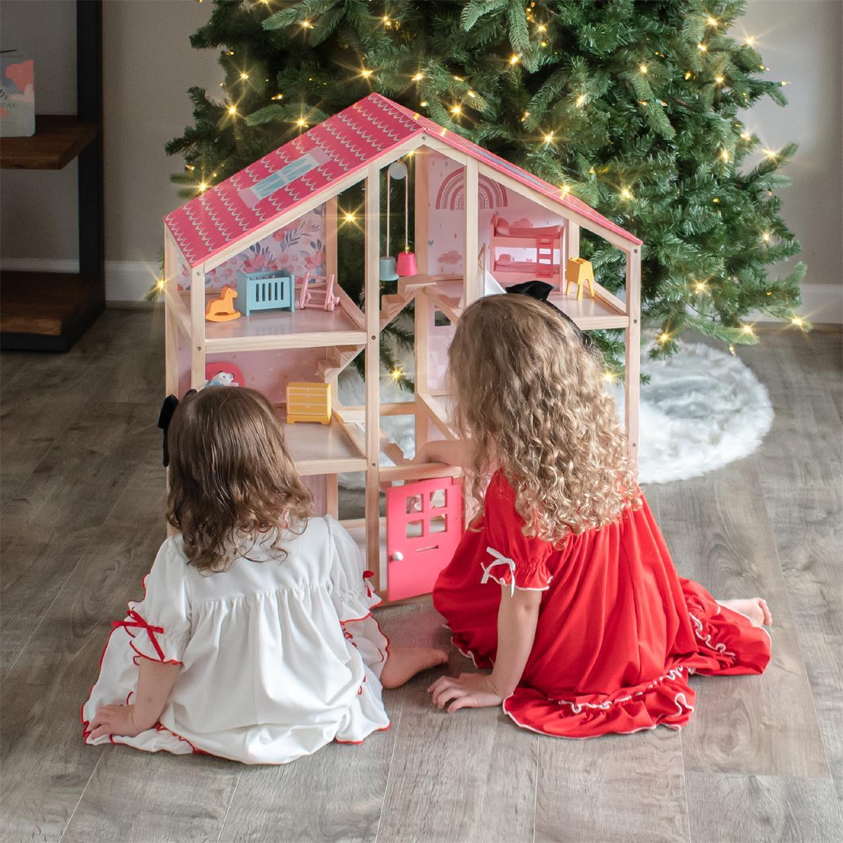 Two children playing with a dollhouse in front of a decorated Christmas tree.