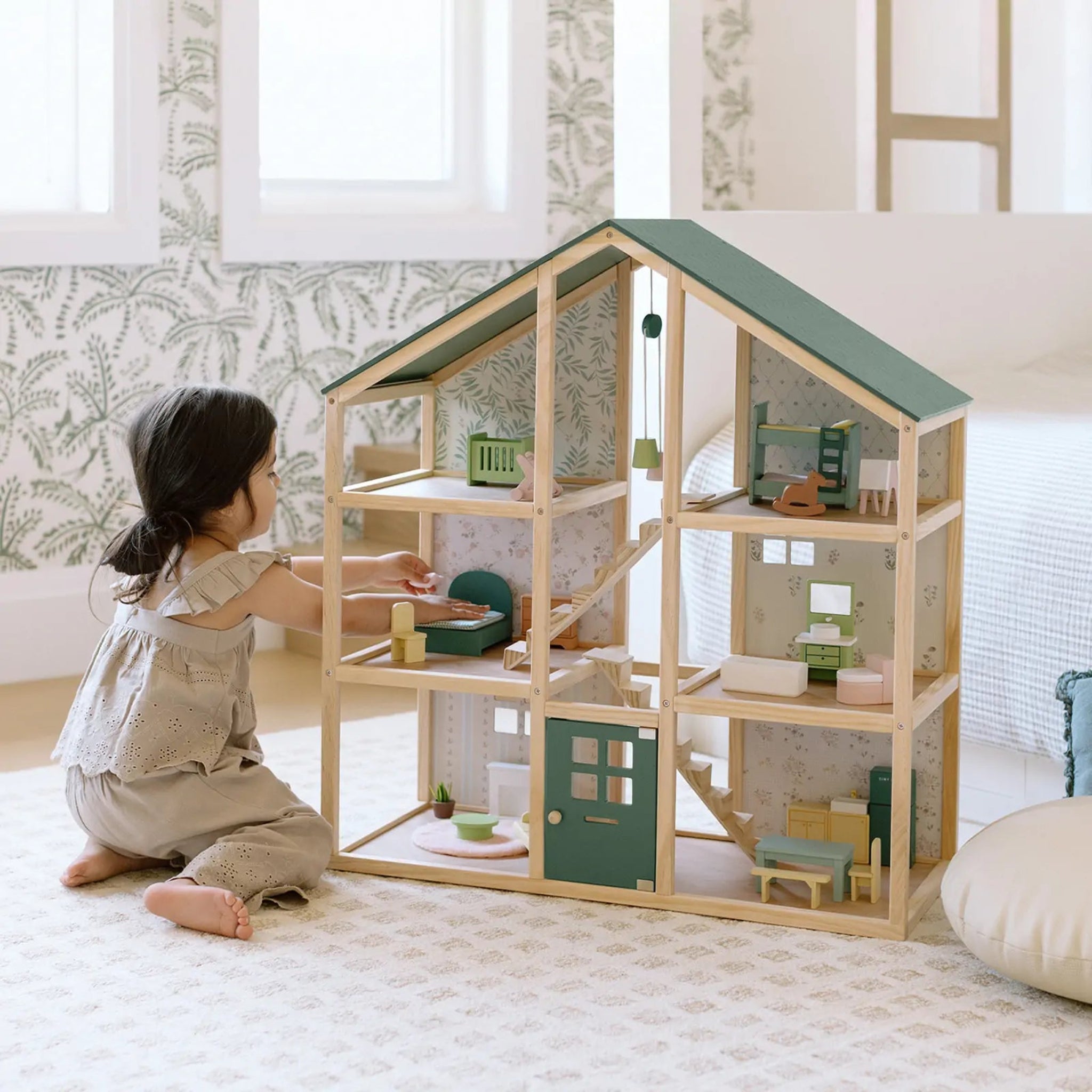 Child playing with a wooden dollhouse in a room with light-colored walls and a rug.