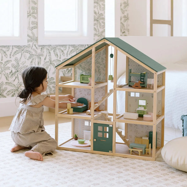 Child playing with a wooden dollhouse in a room with light-colored walls and a rug.