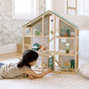 Child playing with a wooden dollhouse in a bright room.