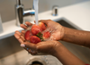 Hands washing strawberries under running water in a kitchen sink.