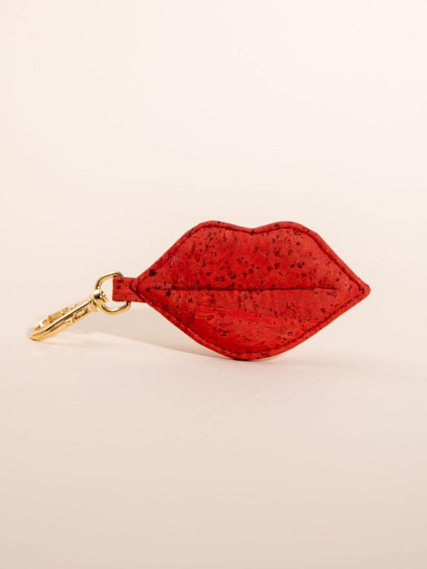Red lip-shaped keychain with gold clasp on a beige background