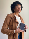Woman wearing a brown coat holding a black book against a plain background