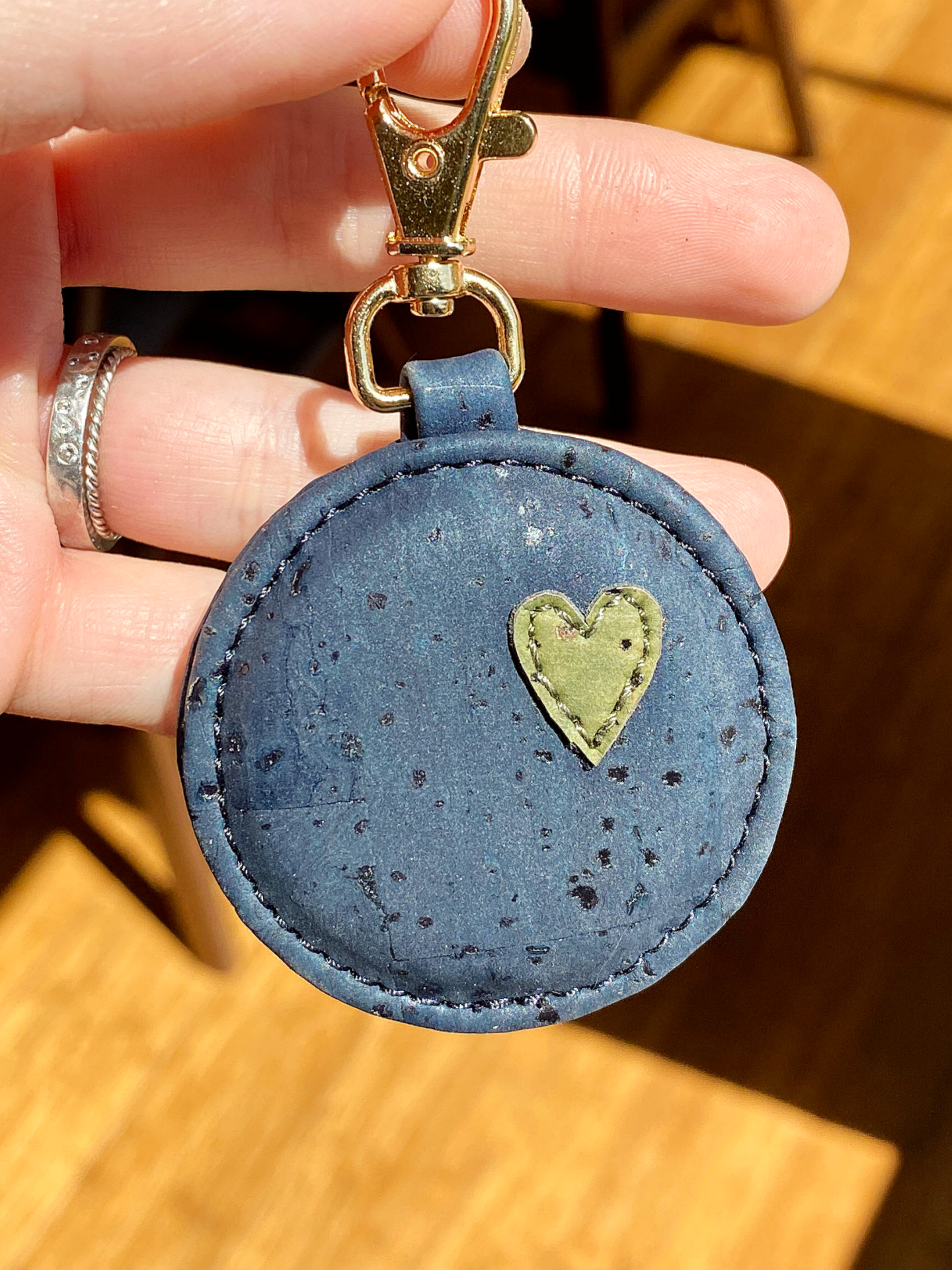 Blue round keychain with a heart design held by a hand on a wooden surface