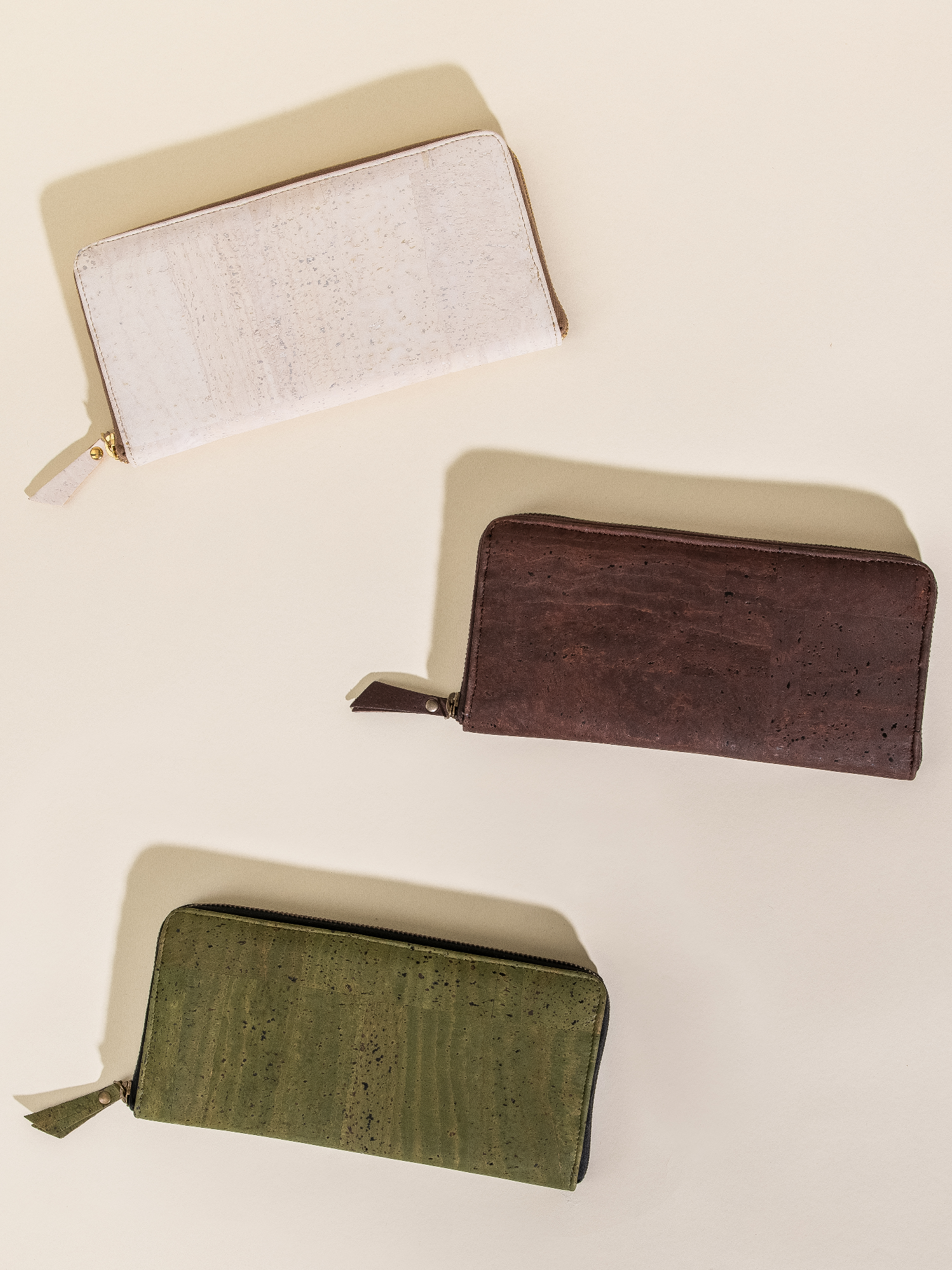 Three wallets in beige, brown, and green on a light beige background