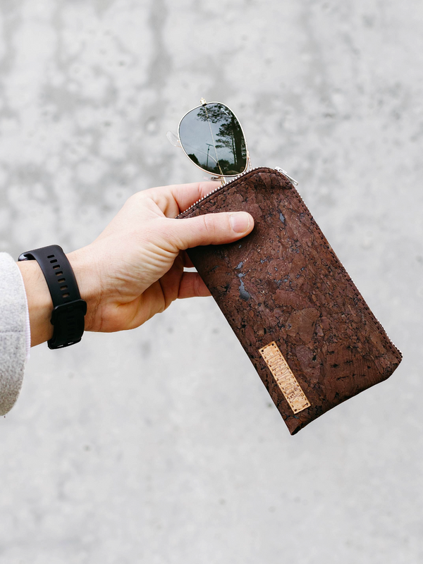 Hand holding a brown cork wallet with a reflective surface on a light gray background