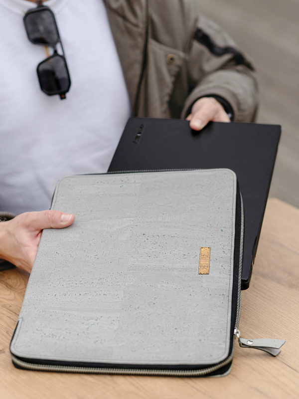 Person holding a gray laptop sleeve and black laptop on a wooden surface.