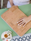 Cork laptop sleeve on a green table with a cup of coffee and saucer.