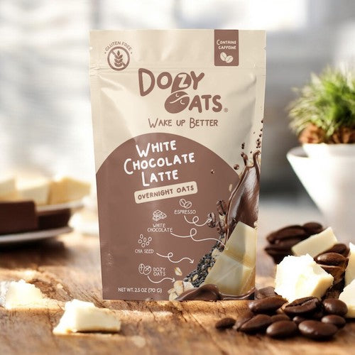 Doby Oats White Chocolate Latte packaging on a wooden surface with coffee beans and white chocolate pieces.