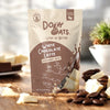 Doby Oats White Chocolate Latte packaging on a wooden surface with coffee beans and white chocolate pieces.
