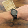 Black wristwatch on a wrist with 'joycoast' branding in the background