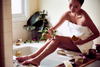 Woman using Desesh metal safety razor and solid shave soap beside a bathtub as part of a sustainable self-care routine