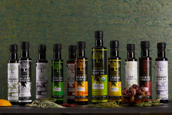 Row of various olive oil and vinegar bottles on a wooden surface with a textured green wall background.