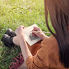 Person sitting on grass drawing in a book