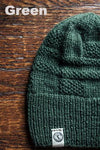 Green knit beanie on a wooden surface with 'Green' text above.