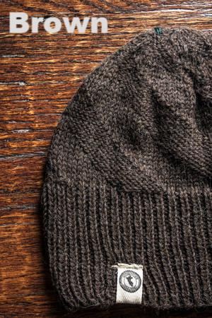 Brown knit beanie with a brand logo on a wooden surface, labeled 'Brown'.