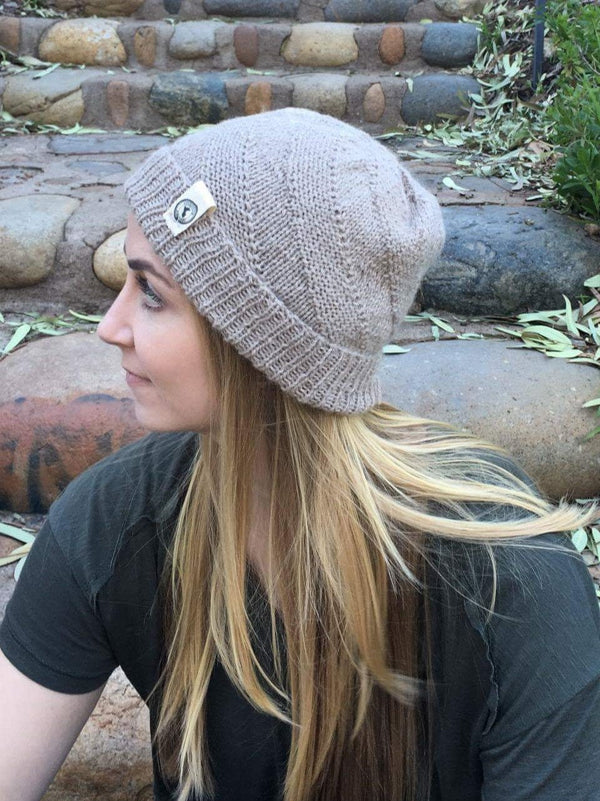 Person wearing a gray knit beanie with a logo, sitting outdoors on stone steps.