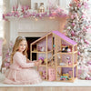 Young girl in a pink dress with a dollhouse and Christmas tree in a decorated room.