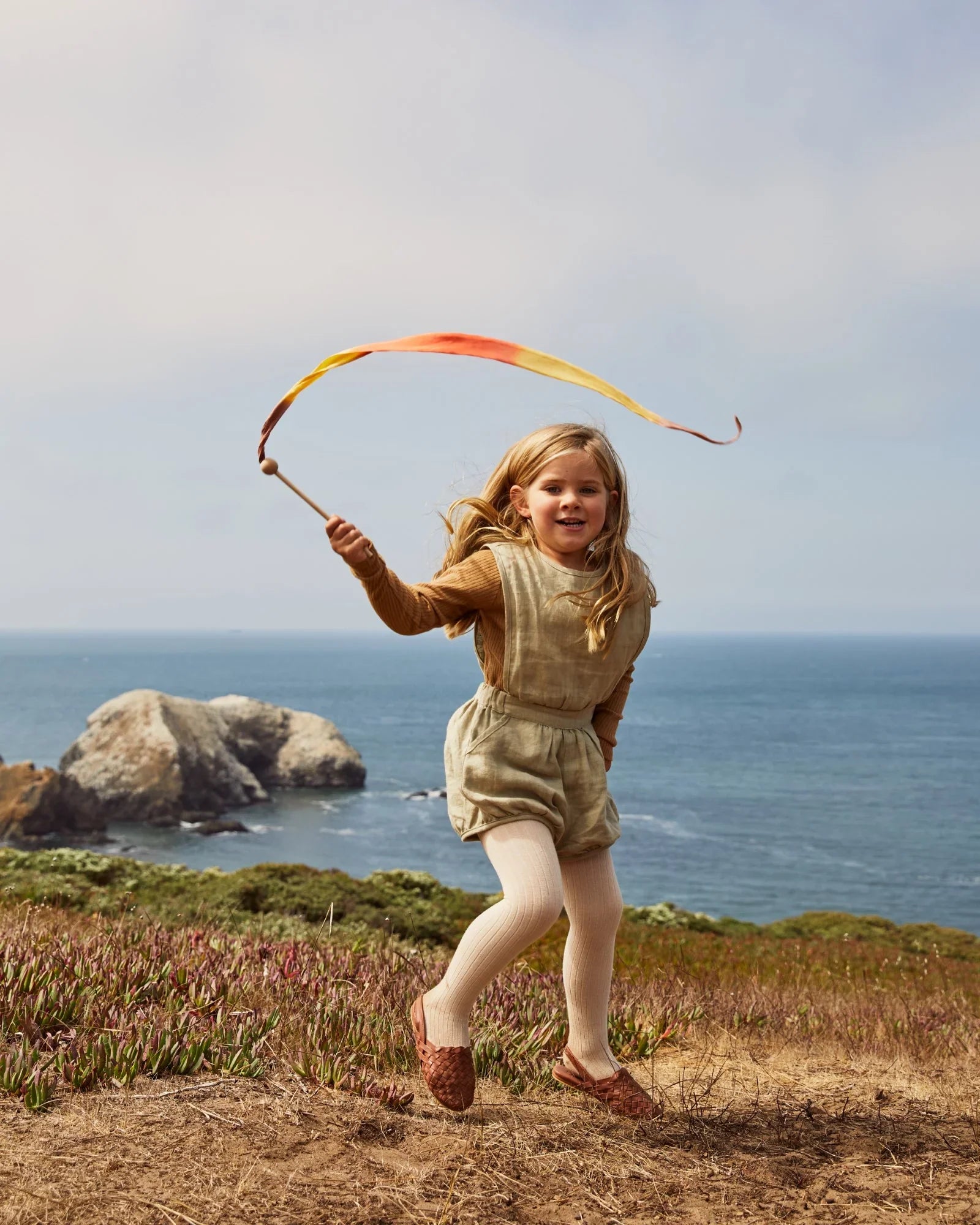 Child playing with a ribbon on a coastal cliffside