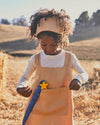 Child in a field wearing a beige apron with a star decoration.