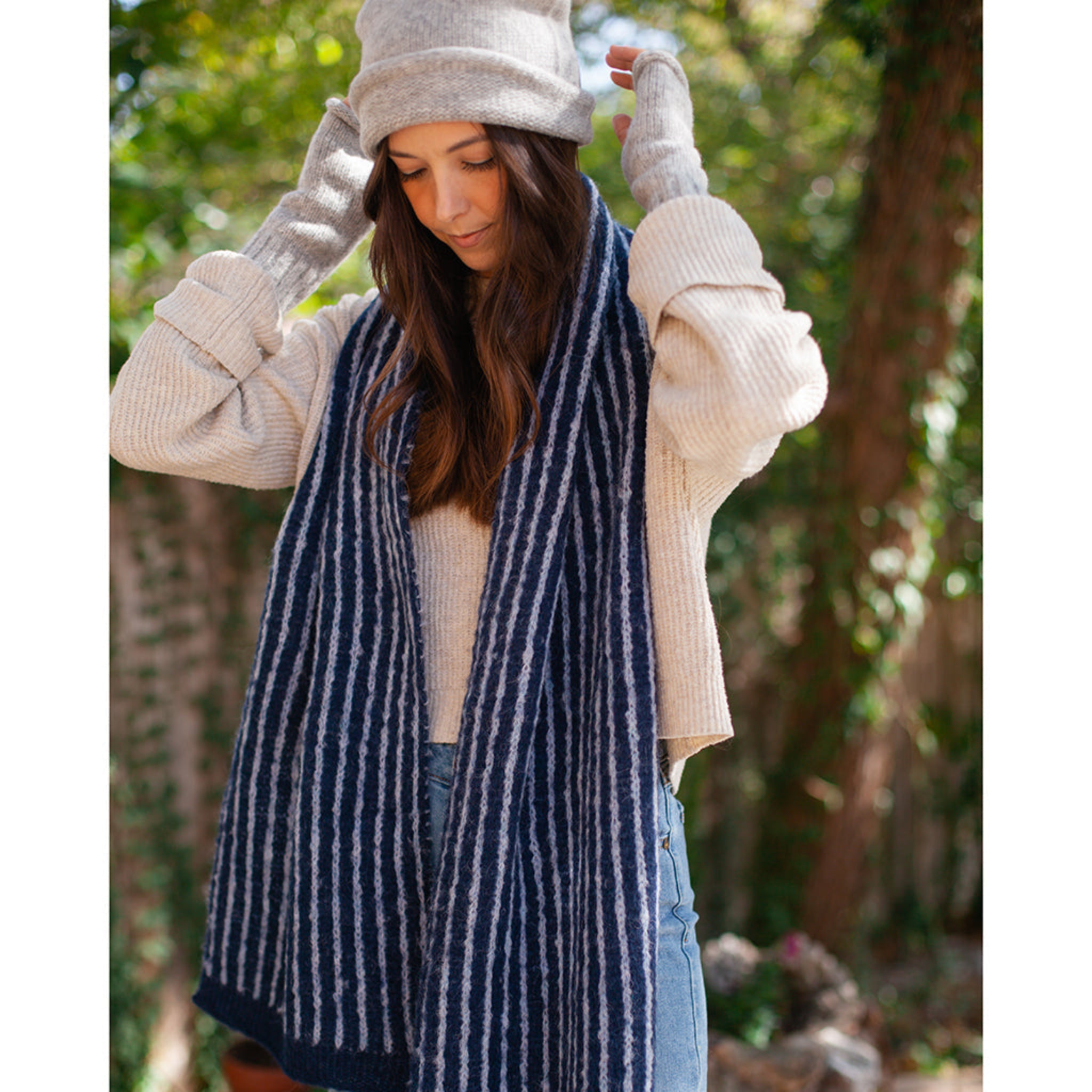 Woman wearing a blue striped scarf, white sweater, and gray beanie outdoors.