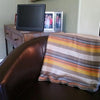 Sofa with a striped blanket draped over it, in front of a wooden cabinet with a television and photos.