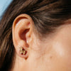 Close-up of an ear wearing a gold llama-shaped earring.