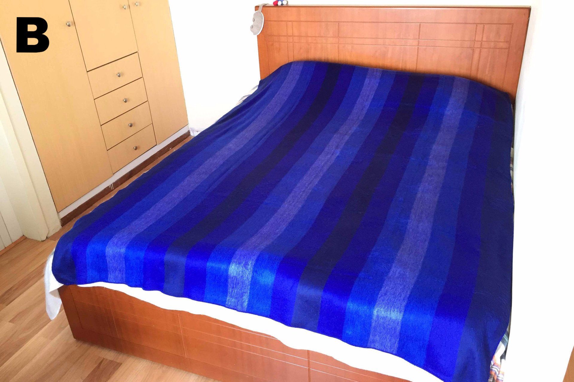 Blue striped bedspread on a wooden bed with a wardrobe in the background