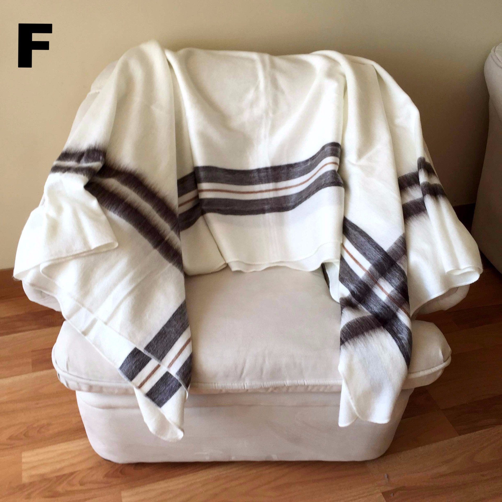 White blanket with brown stripes draped over a white ottoman on a wooden floor.