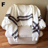 White blanket with brown stripes draped over a white ottoman on a wooden floor.