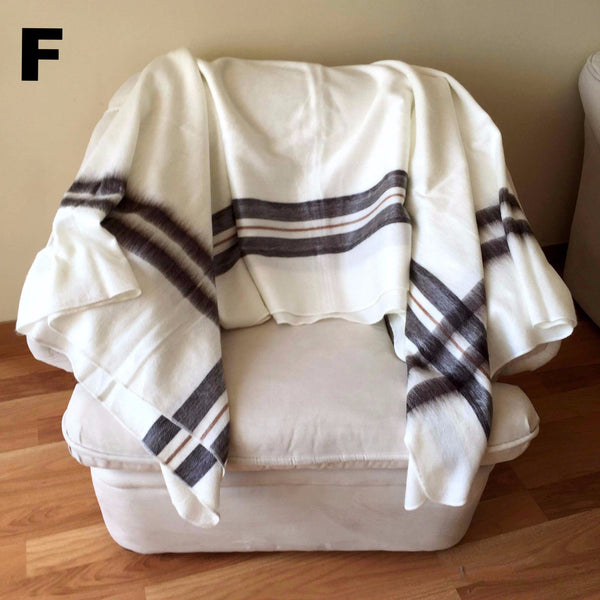 White blanket with brown stripes draped over a white ottoman on a wooden floor.