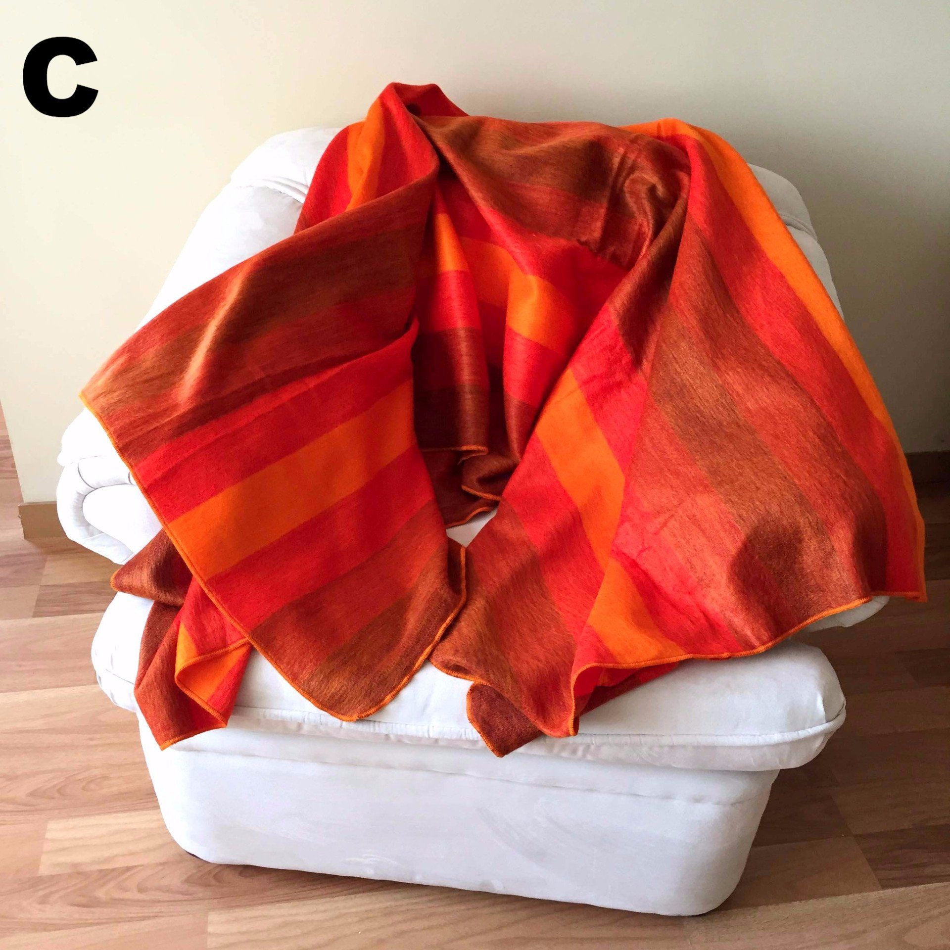 Orange striped blanket draped over a white chair on a wooden floor.